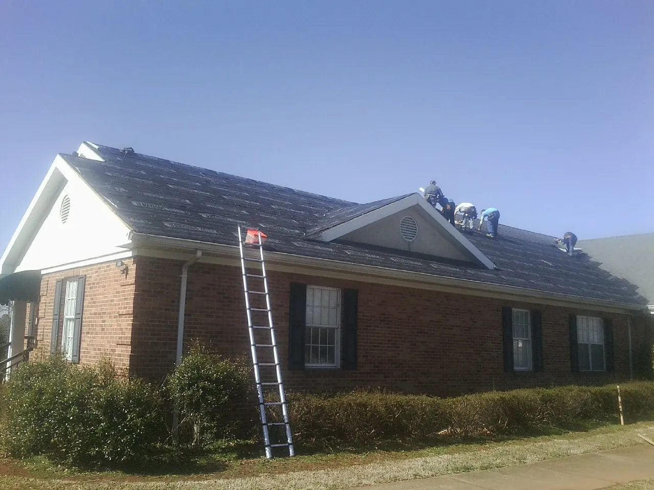 Crew tearing shingles off a brick ranch roof with a ladder set — Metal Roof Repair work by our crew in Leonardville