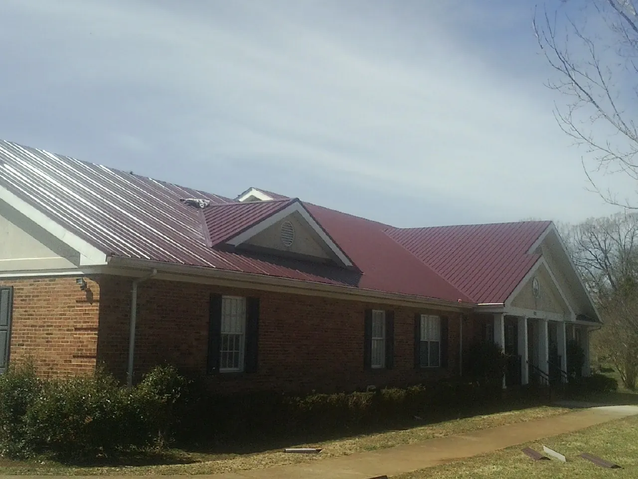 Red metal roof with gabled entries on a long brick building, from a Hail Damage Roof Repair job in Leonardville