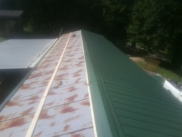 Old rusted panels beside newly installed green metal roofing — Wind Damage Roof Repair by Roofing Brothers in Leonardville