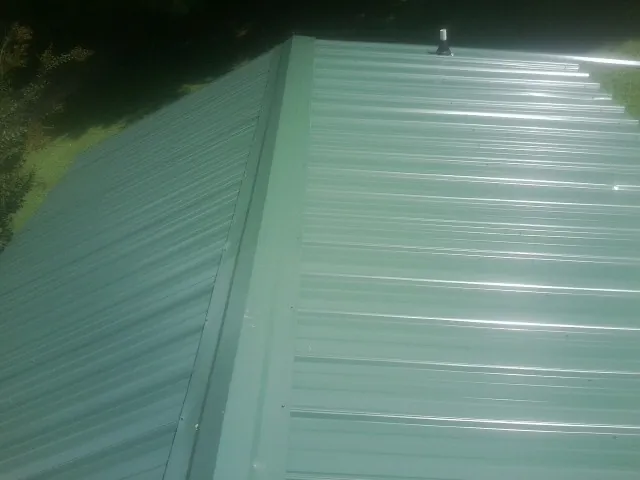 New green metal panels meeting at the ridge of a roof — Flat Roof Repair work by our crew in Leonardville