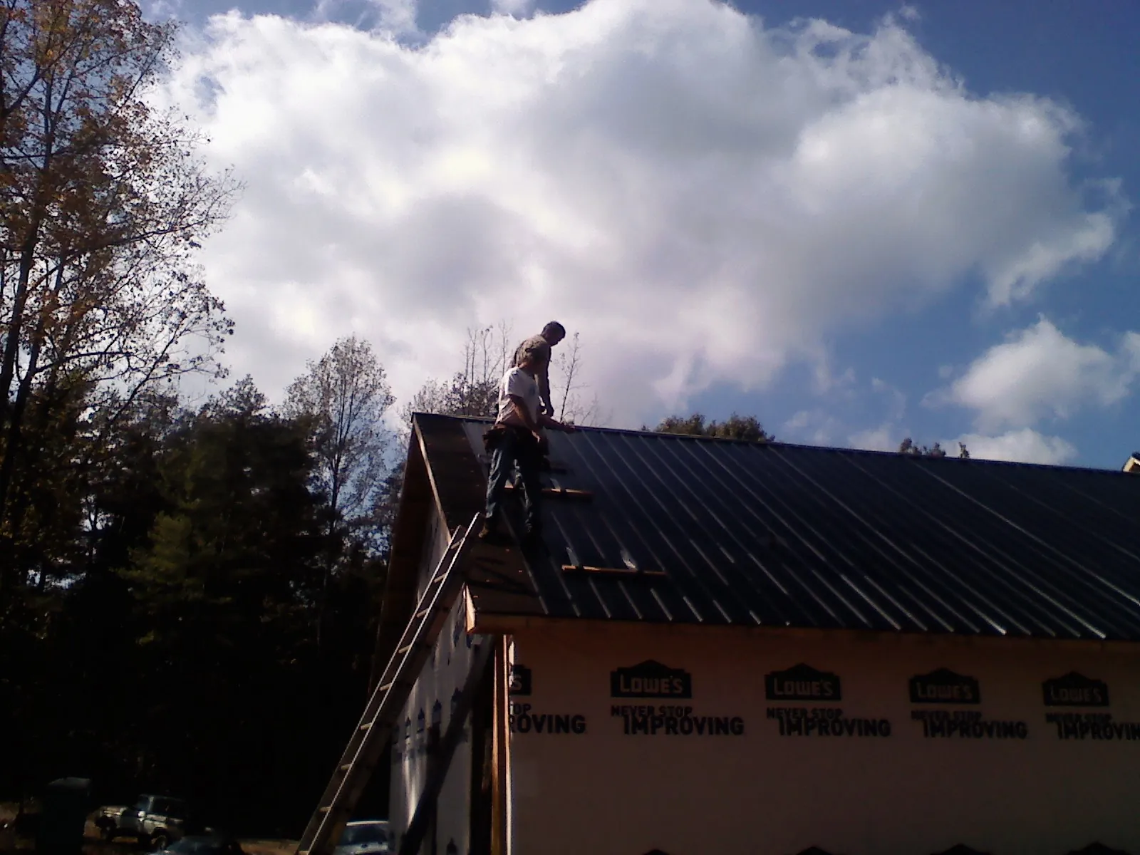 Roofer fastening dark metal panels high against a cloudy sky, from a Roof Inspection job in Leonardville