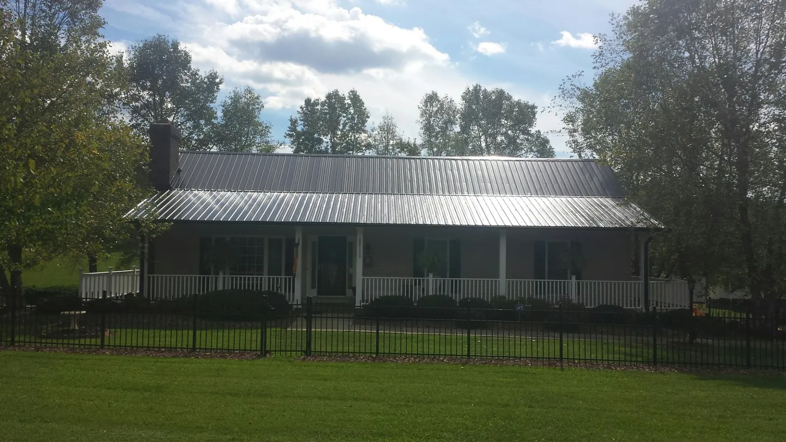 Gray metal roof on a brick ranch with a full width front porch — Gutter Guard Installation work by our crew in Leonardville