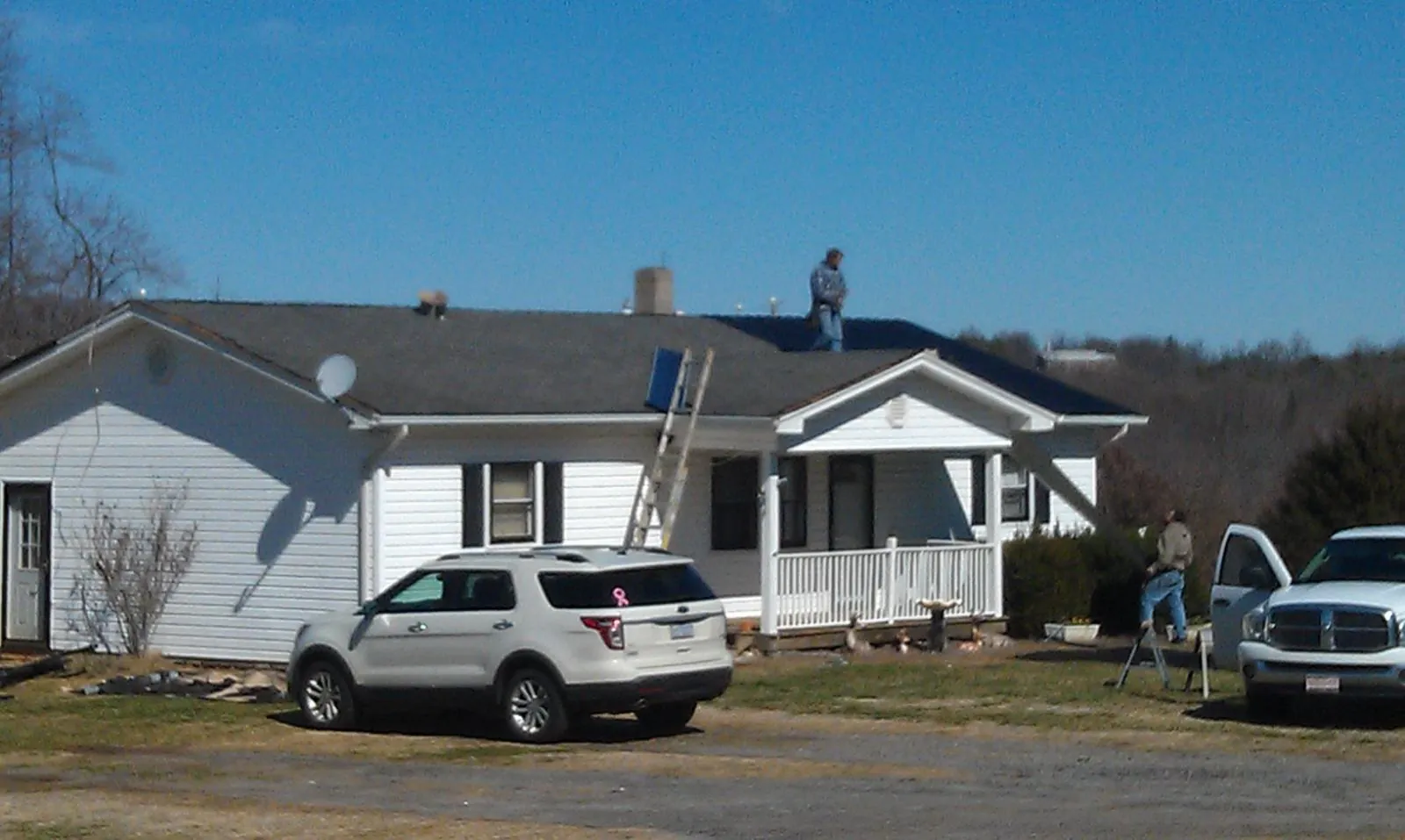 Roofers stripping shingles from a white ranch house roof in Leonardville
