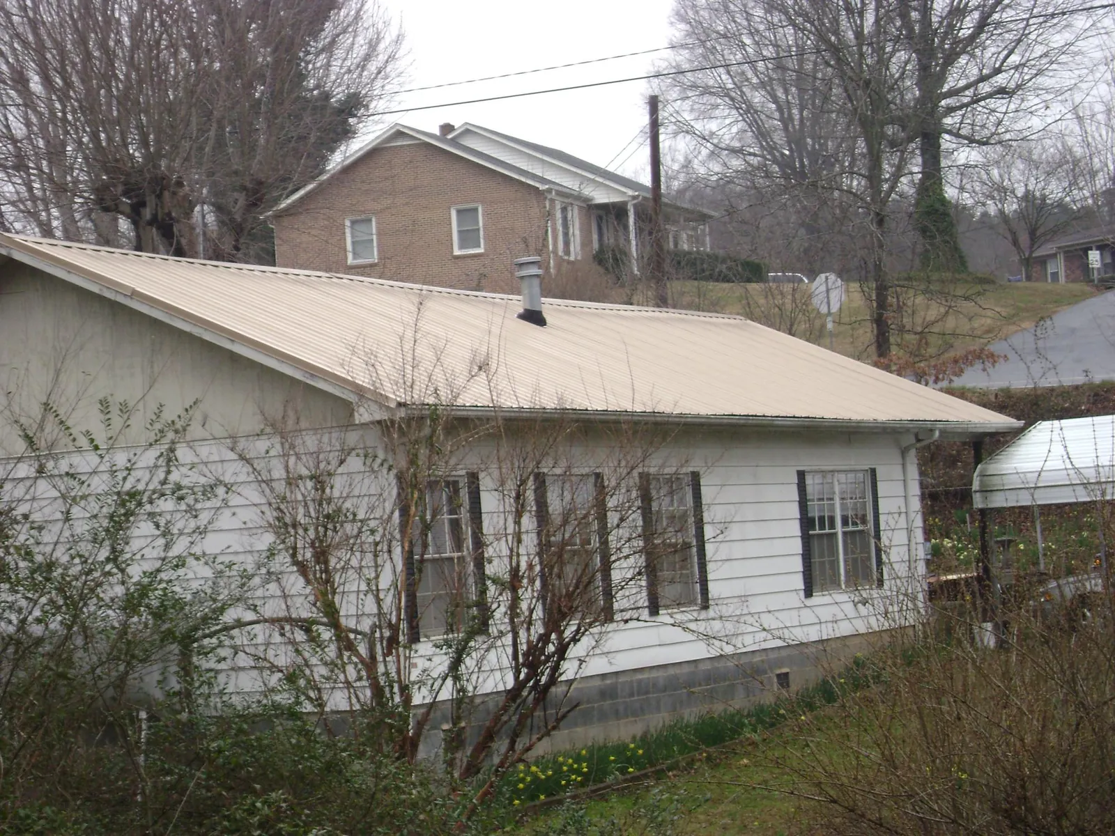 Tan metal roof on a white sided house set into a hillside — Commercial Roofing by Roofing Brothers in Leonardville