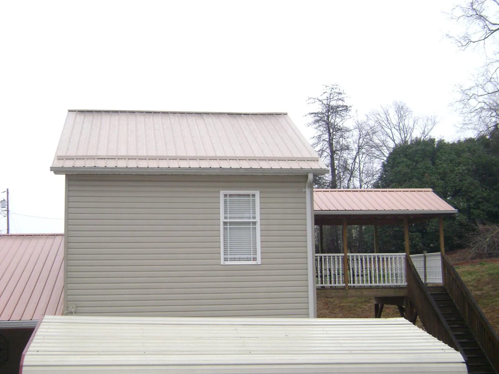 Tan metal roofs on a two story addition and attached porch, from a Roof Replacement job in Leonardville
